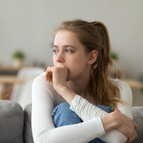 Head shot woman anxious worried woman sitting on couch at home. Frustrated confused female feels unhappy, problems in personal life, quarrel break up with boyfriend and unexpected pregnancy concept